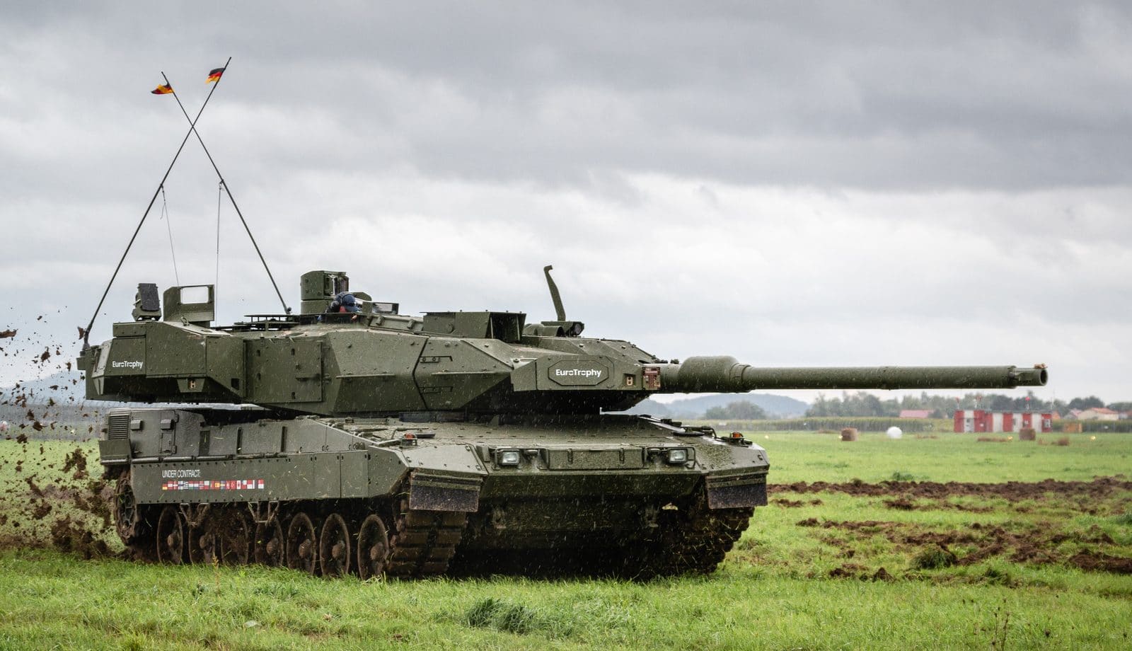 A Leopard 2A7 main battle tank, full side profile, crossing muddy ground during a field demonstration.