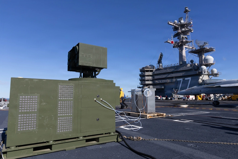 A joint U.S. Navy, Army, and AeroVironment team adjusting a containerized LOCUST laser weapon system aboard the aircraft carrier USS George H.W. Bush during a live-fire test