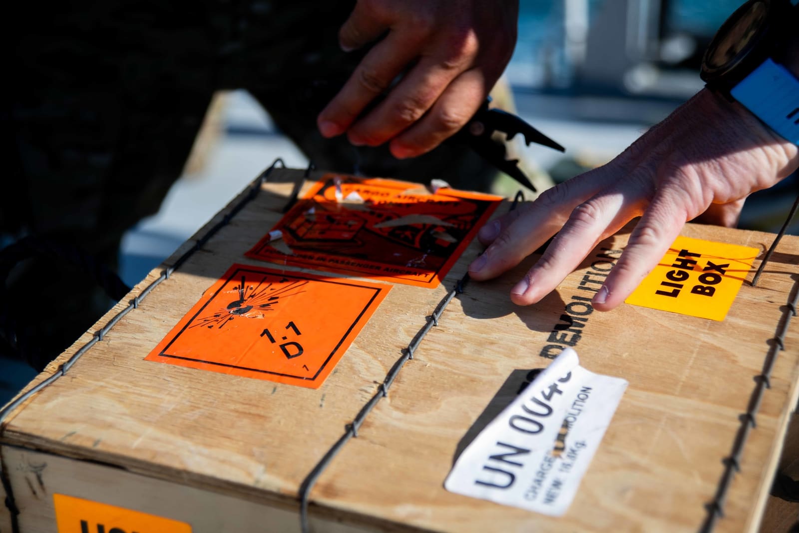 Explosive ordnance disposal technicians handle a hazard-labeled demolition charge crate marked with UN 0044 and explosive warning symbols during a mine countermeasures exercise