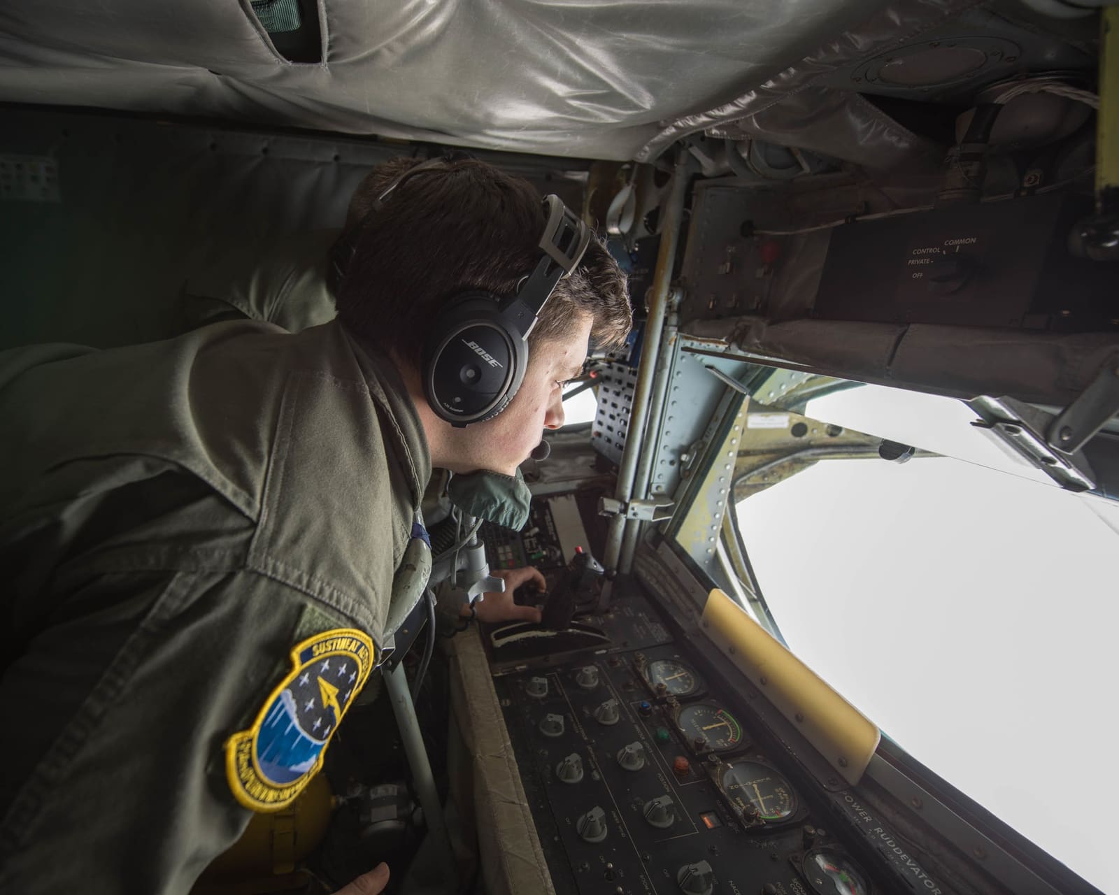 A U.S. Air Force KC-135 Stratotanker boom operator looks through the boom window while preparing to refuel a KC-46 in flight